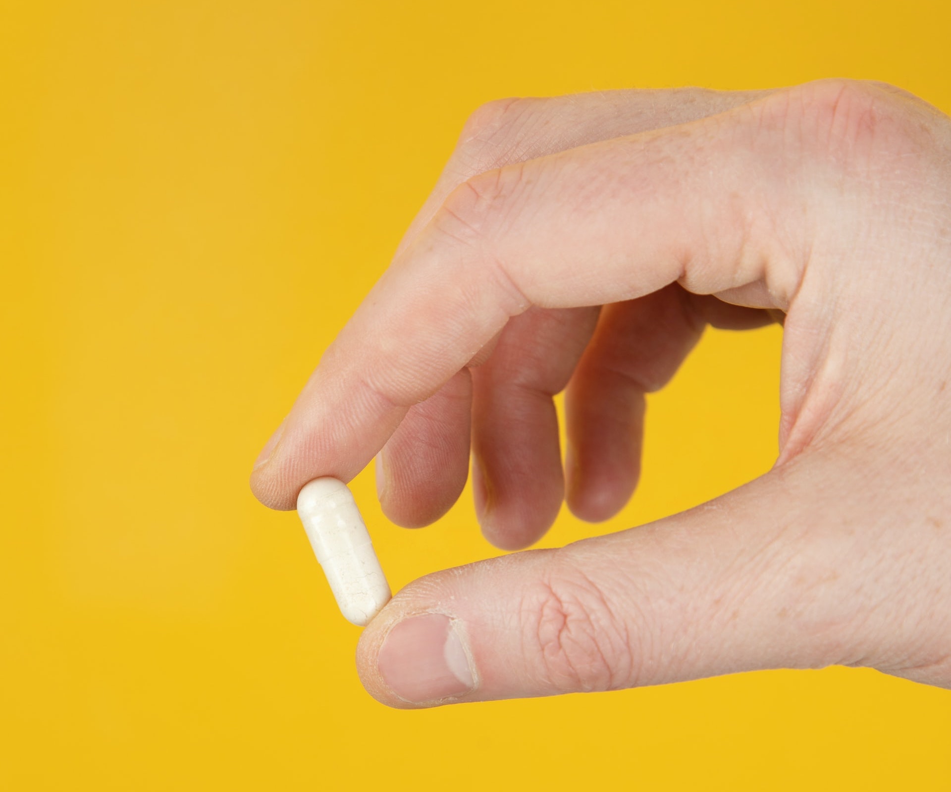 two fingers holding a vitamin capsule against a yellow background