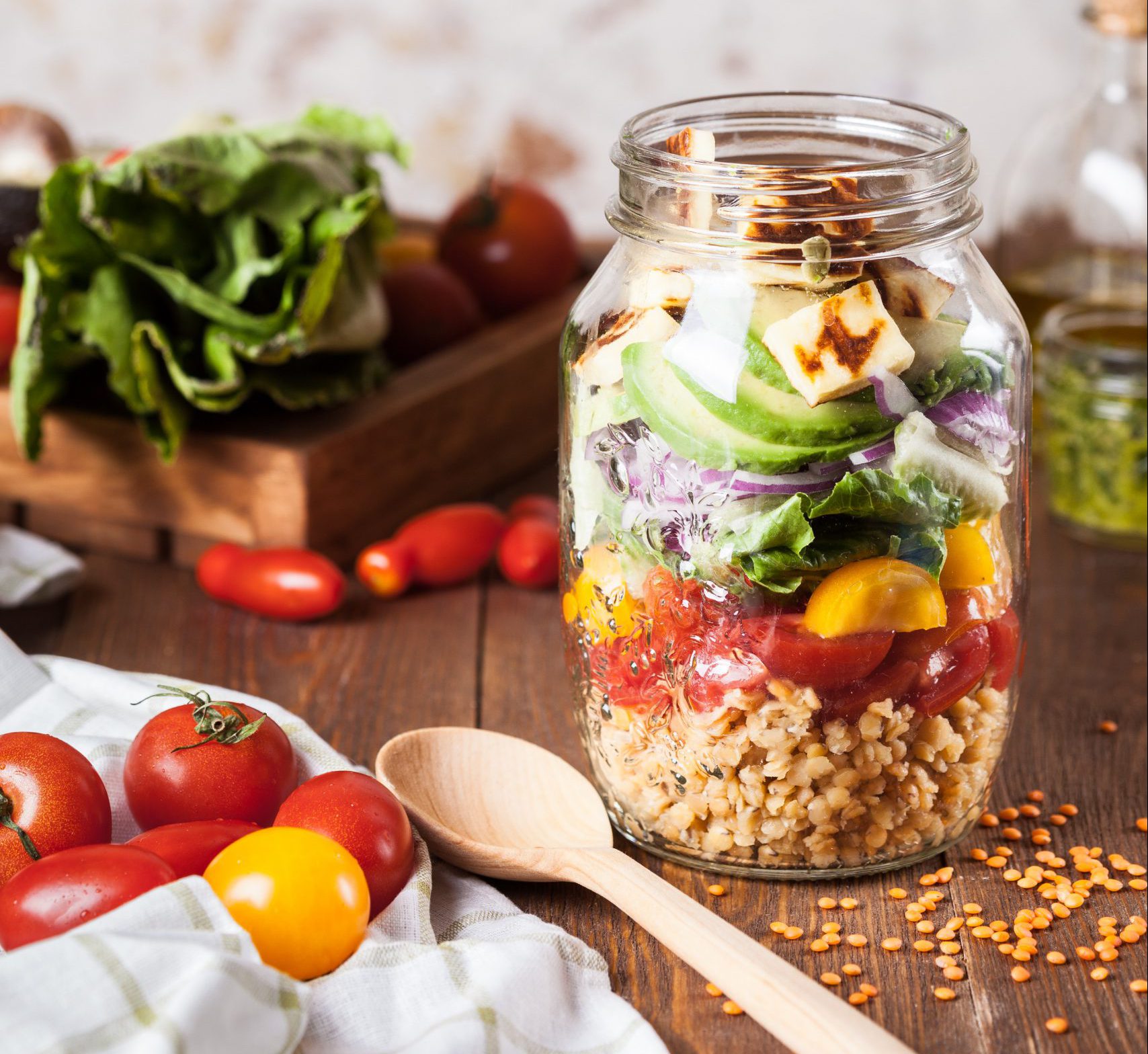 Vegetables in mason jar with wooden spoon and other vegetables surrounding on the table