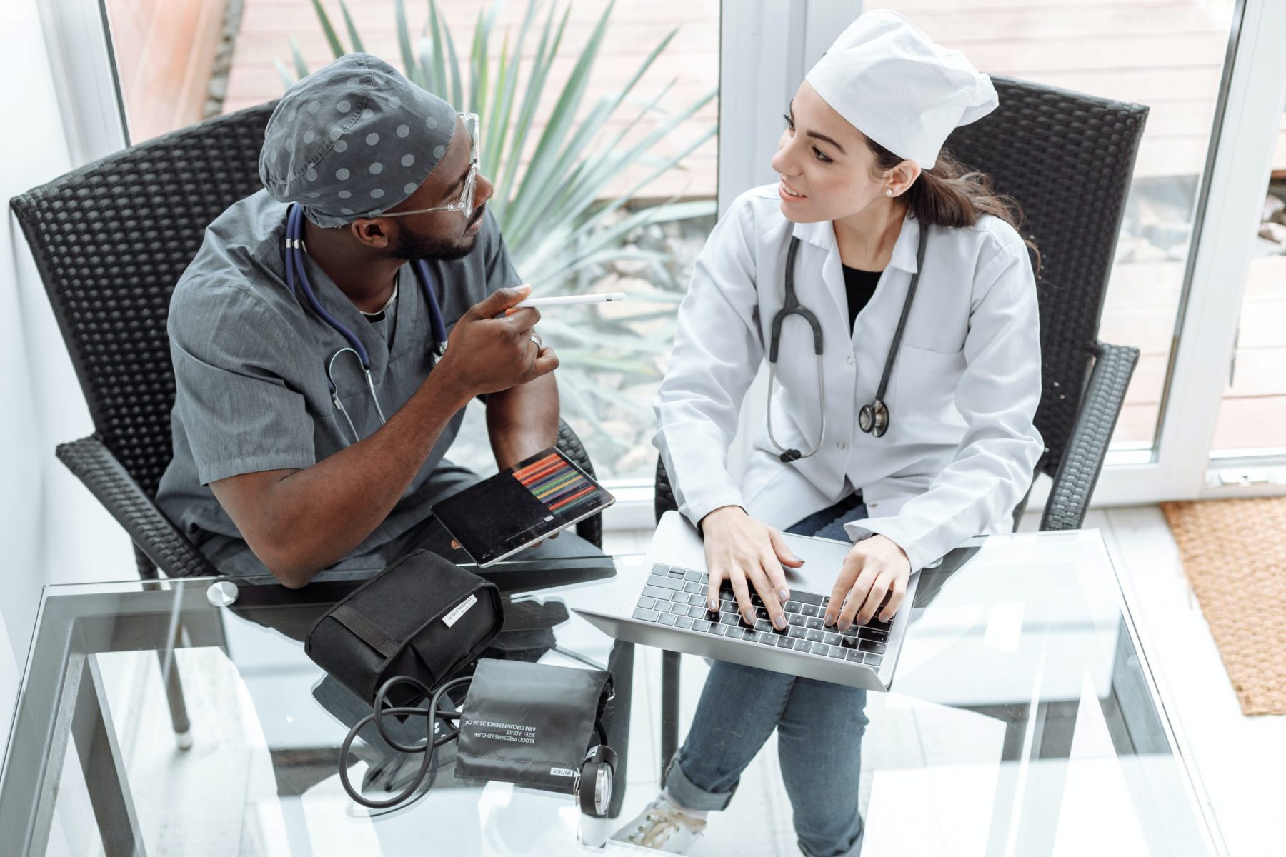 Two doctors sitting at a table with laptop and notes talking