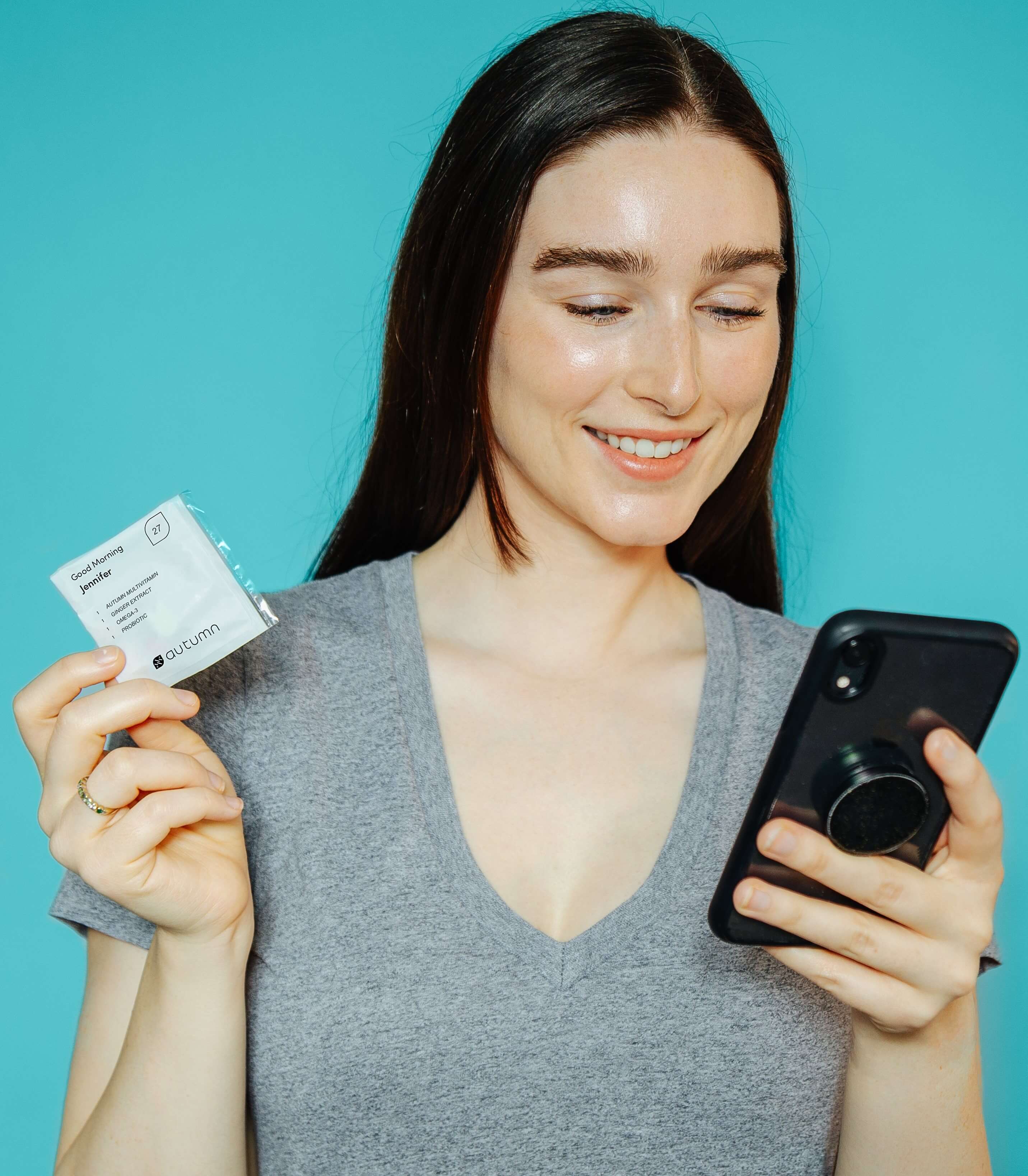 Woman looking at her phone while holding an Autumn DNA customized vitamin packet